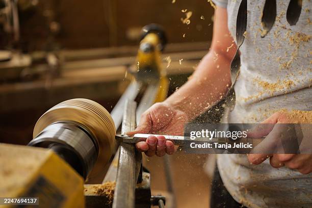 der zimmermann arbeitet sorgfältig mit einer drehbank, formt holz in filigrane muster und erzeugt in einer traditionellen werkstatt voller werkzeuge und handwerkskunst eine sägemehlwolke - drehmaschine stock-fotos und bilder