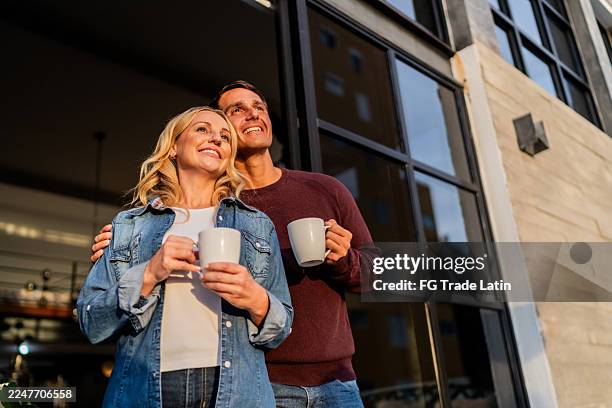 pareja feliz mirando hacia otro lado, relajándose y tomando café por la mañana en casa - pareja de mediana edad fotografías e imágenes de stock