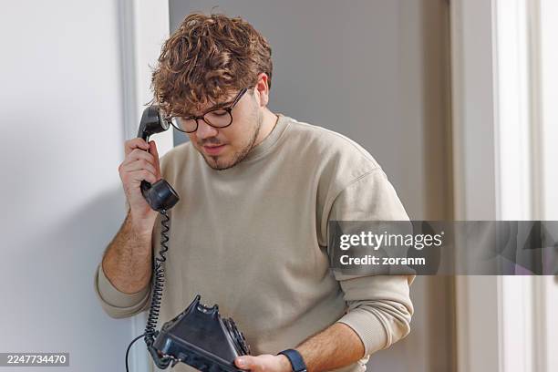 portrait of teenage boy holding rotary phone and talking on landline phone receiver at home - telefone fixo imagens e fotografias de stock