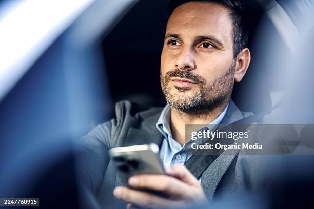 businessman sitting in car using smartphone distracted driving - drivers seat stock pictures, royalty-free photos & images