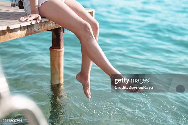 woman splashing water with her feet in the sea from a dock - leg stock pictures, royalty-free photos & images