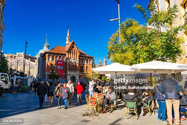 tourists enjoying an autumnal sunny day near central market in valencia-spain. sitting at sidewalk café and walking in the city. famous place visited by tourist and locals - historic building stock pictures, royalty-free photos & images