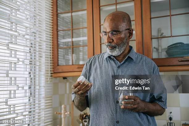 senior indian man reading medication label at home – kuala lumpur - tomar remédio imagens e fotografias de stock
