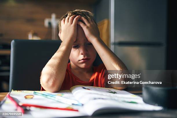 boy with head in hands at desk looking frustrated during homework at home - dislessia foto e immagini stock