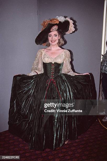 American actress Sharon Wyatt wearing period costume featuring a green corset and full skirt and a wide-brimmed hat with feathers, 1985.