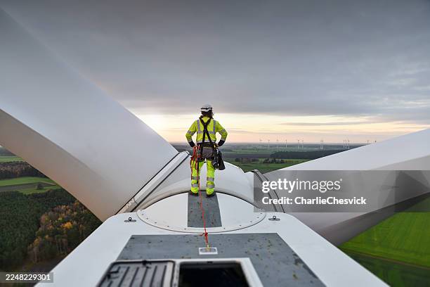 back view on rope access technician standing on roof (hub) of wind turbine and looking at sunrise - renewable energy stock pictures, royalty-free photos & images