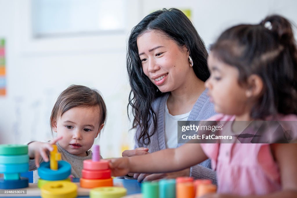 Asian Mother With Two Children Playing With Colorful Stacking Toys In Bright Classroom