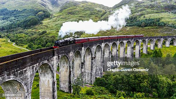 vista aérea del viaducto de glenfinnan con tren de vapor que cruza arcos de piedra históricos en las tierras altas de escocia, hito turístico icónico rodeado de verdes colinas y paisajes de valles, concepto de turismo y patrimonio - puente de ferrocarril fotografías e imágenes de stock