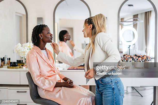 kosmetikerin entfernt fehler auf den lippen einer jungen schwarzen kundin mit einem wattestäbchen im schönheitssalon - permanent make up stock-fotos und bilder