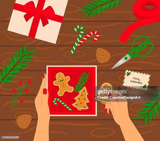hands preparing christmas gifts with gingerbread cookies and christmas decorations. high angle view of wooden table with fir tree branches, pine cones and candy canes - christmas cookie tin stock illustrations