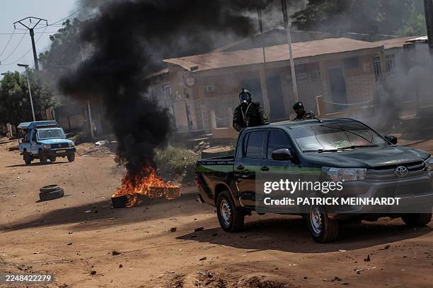 Guinea Bissau security forces patrol cars drive near burning tyres in the area of incidents with protestors in Bissau on Novmeber 29, 2025.