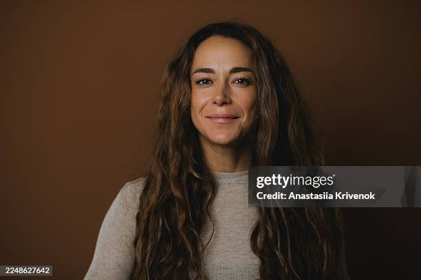 confident woman with long wavy hair in beige sweater against warm brown studio background - wavy hair stock pictures, royalty-free photos & images