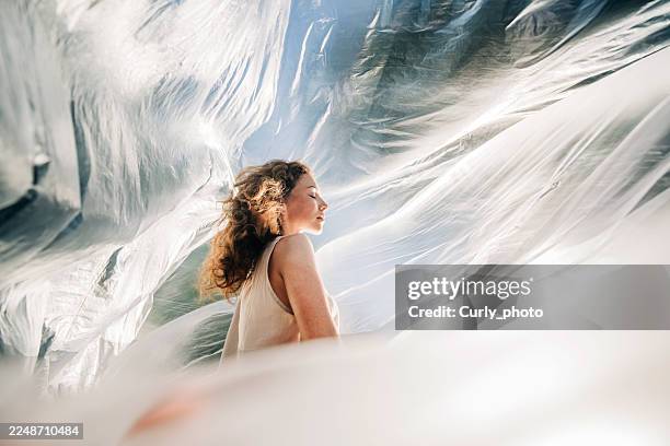 profile of a woman with closed eyes surrounded by illuminated translucent plastic sheets. the ethereal light evokes a sense of serenity, environmental awareness, and artistic beauty. - harmony stock pictures, royalty-free photos & images