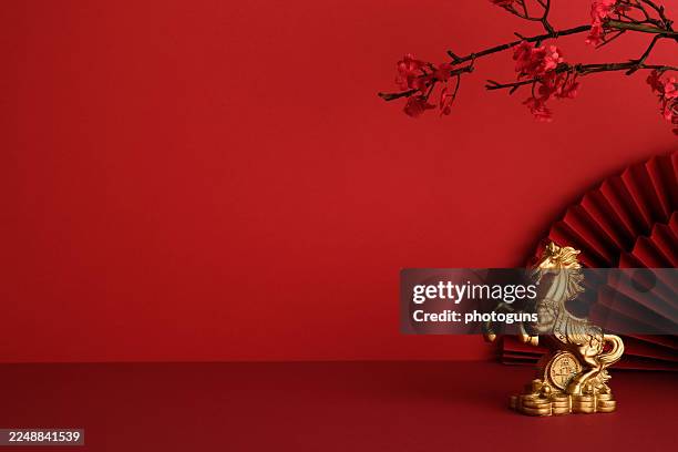 Golden horse statue next to a red folding fan on a red background with copy space. Happy Chinese New Year 2026, year of the fire horse.