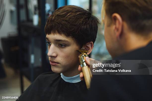 young man getting haircut with electric clippers in a modern barbershop - hair clipper stock pictures, royalty-free photos & images