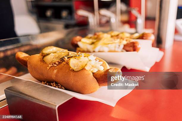 close-up of fresh hot dogs topped with pickles arranged on food truck - fast food stock pictures, royalty-free photos & images