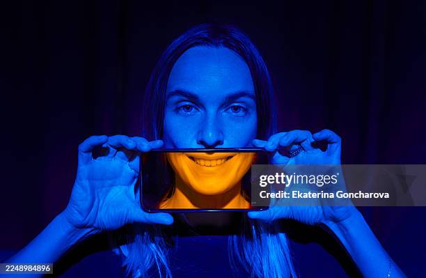 woman holding smartphone under blue and orange lighting, creating playful, creative portrait - vingança imagens e fotografias de stock