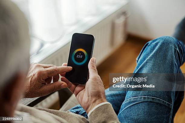 senior man using smart home thermostat application on phone - electric skateboard stock pictures, royalty-free photos & images