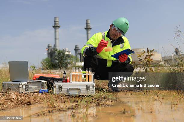 an environmental engineer wearing green safety gear is sampling and testing water around the factory - sample holder stock pictures, royalty-free photos & images
