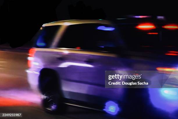 view of police vehicle with lights flashing as it races along road at night - responsabilidad policial fotografías e imágenes de stock