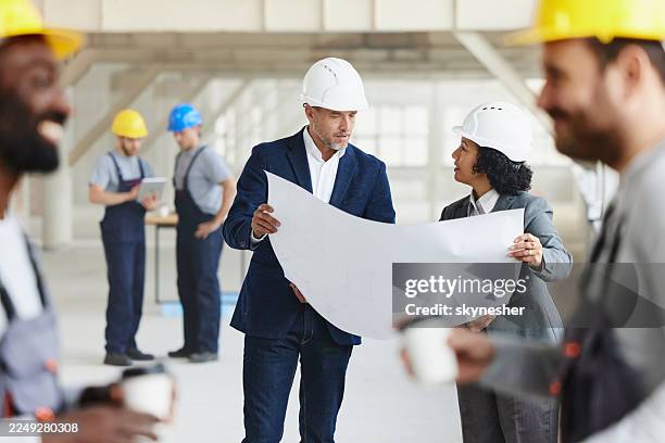project managers examining blueprints at construction site. - real estate developer stock pictures, royalty-free photos & images