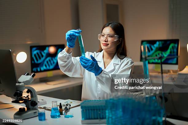 young adult woman scientist working in a modern laboratory, holding a test tube with blue liquid, researching genetics and chemistry - laboratory glassware stock pictures, royalty-free photos & images