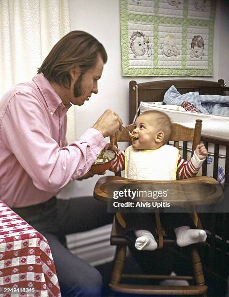 Father feeds son in high chair in Minneapolis, Minnesota in 1975.