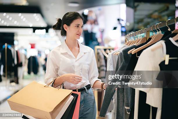 smiling young woman holding shopping bags in a clothing store at a modern shopping mall - accro du shopping photos et images de collection