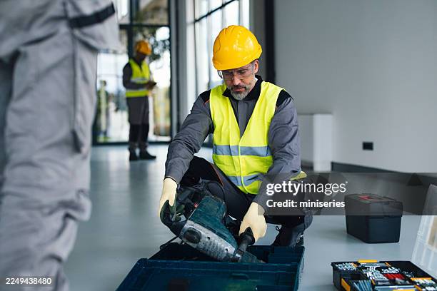 construction worker in neon vest and hard hat works with tools in new office renovation project - elektrisch gereedschap stockfoto's en -beelden