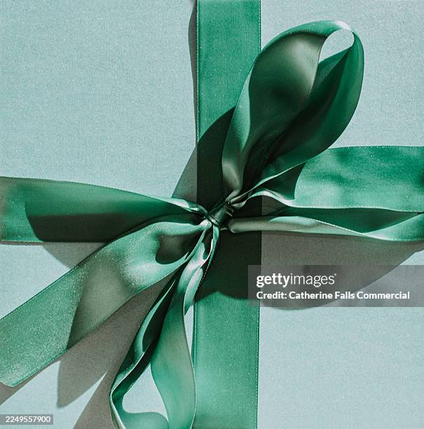 top down close up of a large green tied ribbon bow on top of a blue gift box - gift lounge stock-fotos und bilder