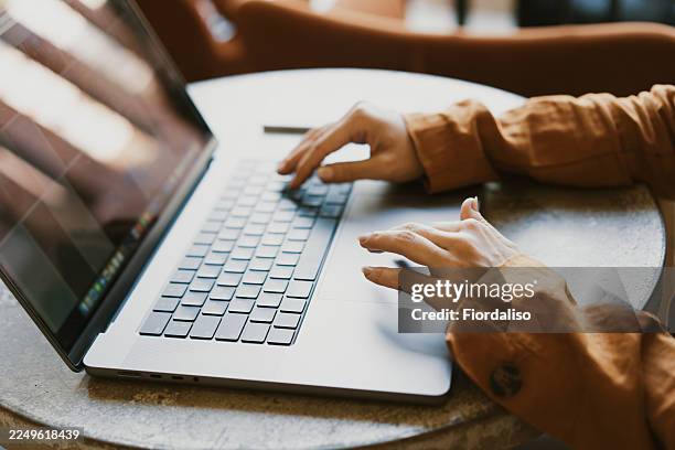 person typing on a laptop at a round table in a cozy workspace, focused on work - websurfen stock-fotos und bilder