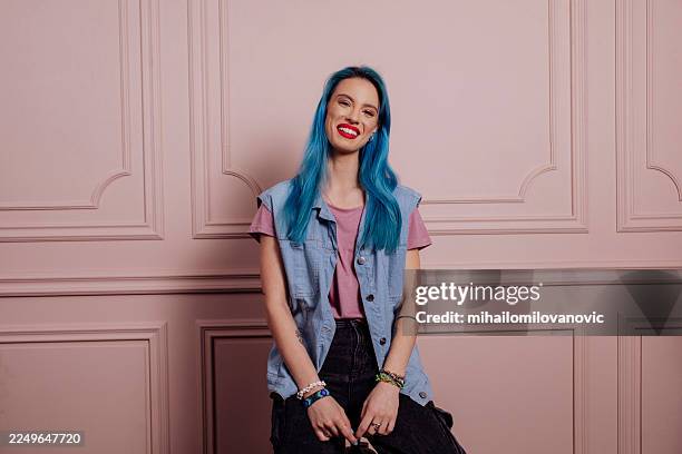 bunt gekleidete frau mit blauen haaren posiert in lässigem straßenstil an der rosa wand - blaues haar stock-fotos und bilder