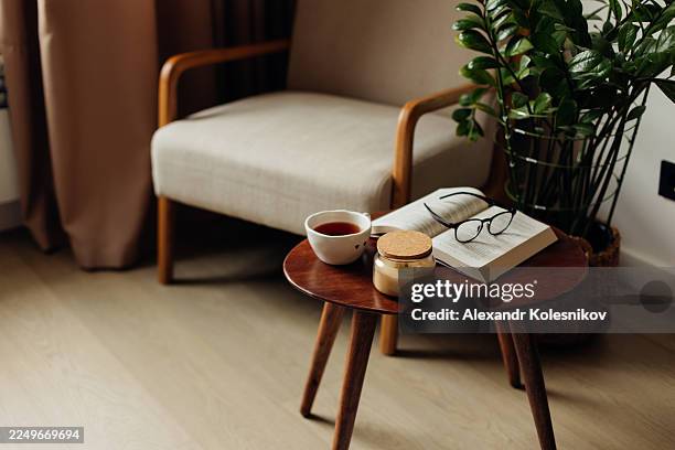 cozy reading nook with glasses on open book, tea, and jar on wooden table - side table stock pictures, royalty-free photos & images