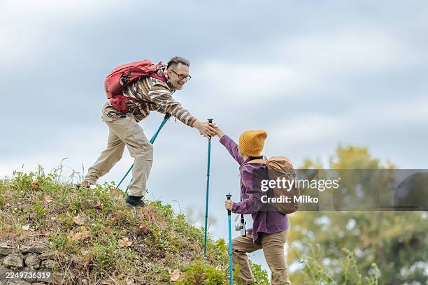 adventurous couple hiking together on a trail with trekking poles and backpacks - hiking pole stock pictures, royalty-free photos & images