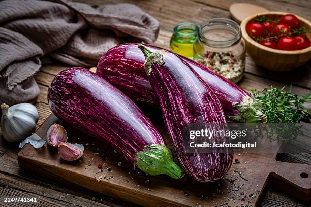 melanzane viola biologiche intere su un tagliere. cucina o cucinare verdure fresche, pasti sani o cibo crudo. erbe aromatiche e condimenti - melanzana foto e immagini stock