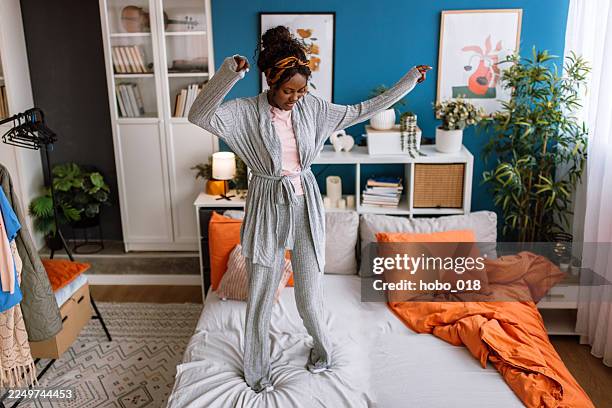 happy smiling black woman in pajamas having fun while jumping on a bed in the morning. - nachtkleding stockfoto's en -beelden