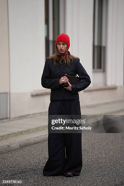Sina Anjule is seen wearing a navy pinstripe wool blazer featuring a tailored and slightly cropped silhouette with structured shoulders, a sculpted...