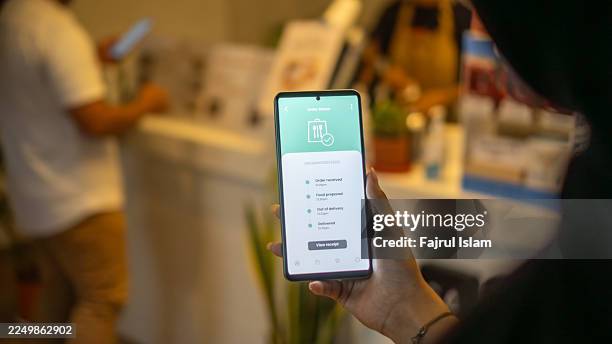 over the shoulder view of young asian woman using meal delivery service and ordering food online with smartphone - kontakfreie anlieferung stock-fotos und bilder