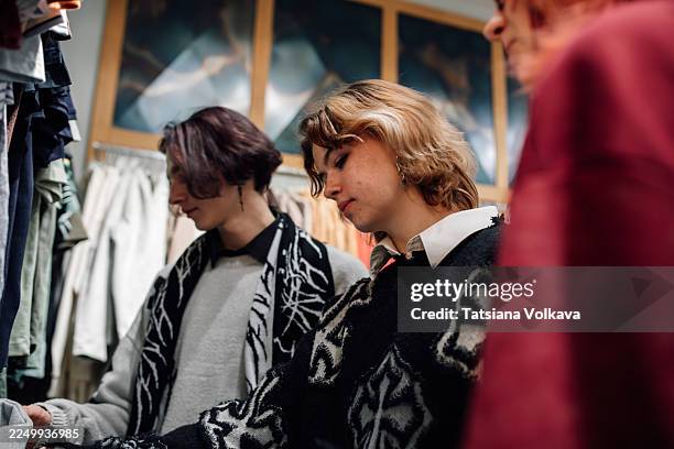 friends shopping for knitwear in a cozy fabric store with patterned sweaters - fast fashion stock pictures, royalty-free photos & images