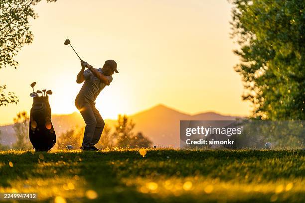caucasian male golfer in mid-swing enjoying evening game on sunlit course - golf stock pictures, royalty-free photos & images
