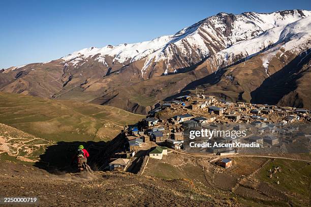 mountain biker rides down mountain slope to village - azerbaijan stock pictures, royalty-free photos & images