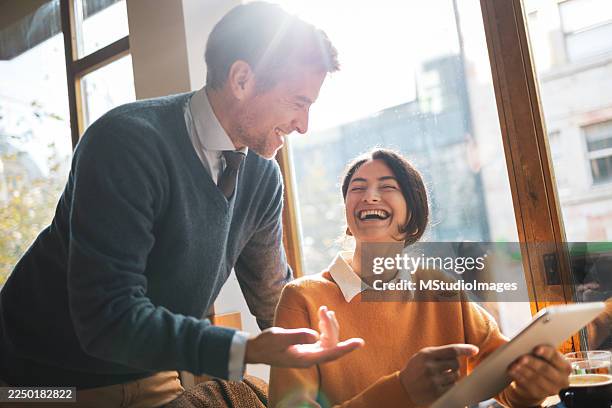 colleagues laughing using digital tablet in cafe - simplify work stock pictures, royalty-free photos & images