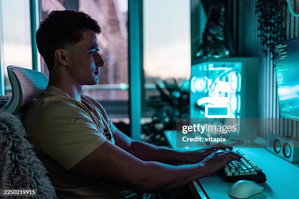 joven jugador enfocado en un escritorio de ordenador iluminado en azul en una configuración moderna de juegos - alfombra raton fotografías e imágenes de stock