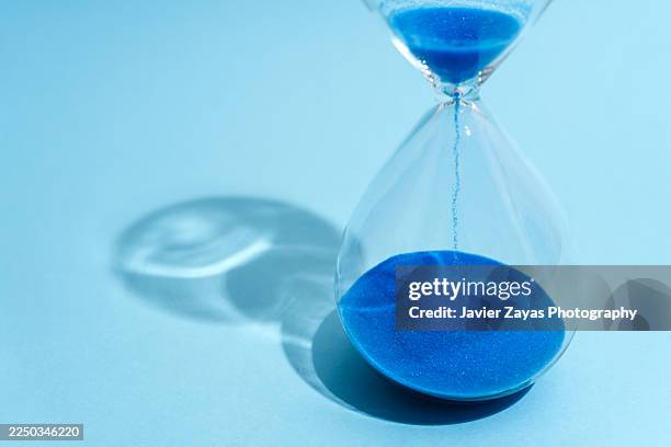 blue sand running through hourglass measuring passing time - frist stock-fotos und bilder