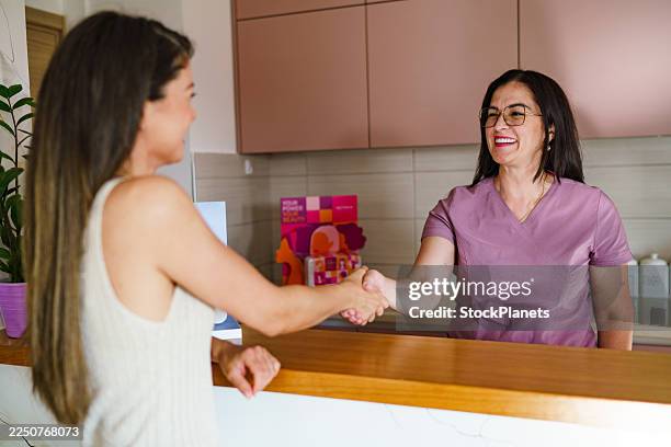 clinic receptionist welcoming client with a friendly handshake. - spa reception stock pictures, royalty-free photos & images
