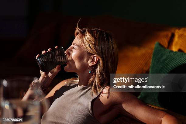 woman relaxing at home, drinking from glass tumbler - thirsty stock pictures, royalty-free photos & images