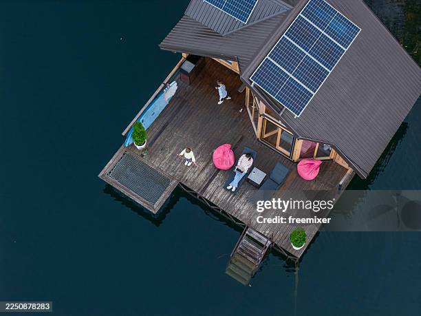 aerial view of a modern lakeside house with solar panels and relaxed group on the deck - recreational boat stock pictures, royalty-free photos & images