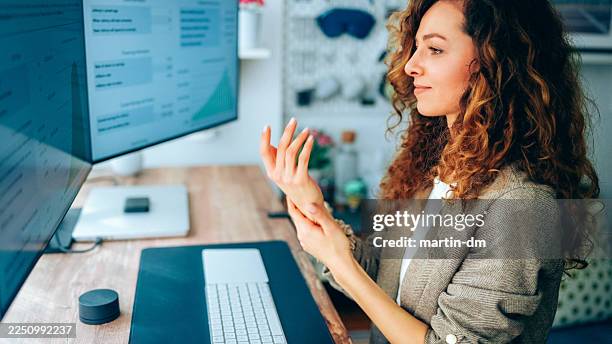 businesswoman using hand cream while working at standing desk in modern home office - shea butter stock pictures, royalty-free photos & images