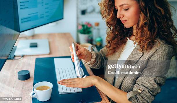 businesswoman using hand cream while working at standing desk in modern home office - shea butter stock pictures, royalty-free photos & images