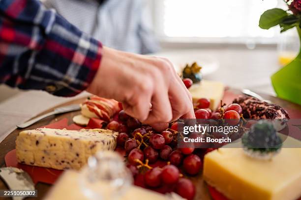 man takes grapes from cheese board on thanksgiving - grazing table stock pictures, royalty-free photos & images